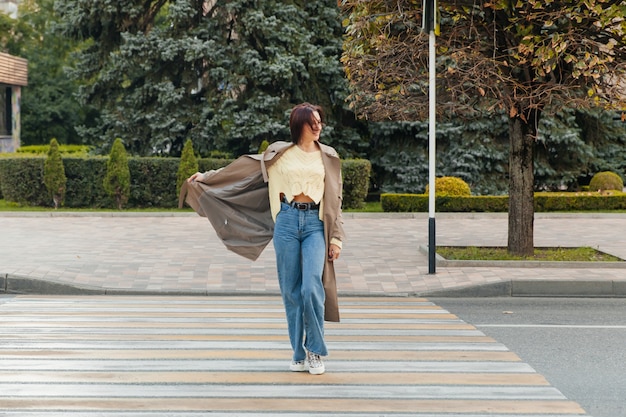 Business woman in a long raincoat crossing the road on the street in sunny weather