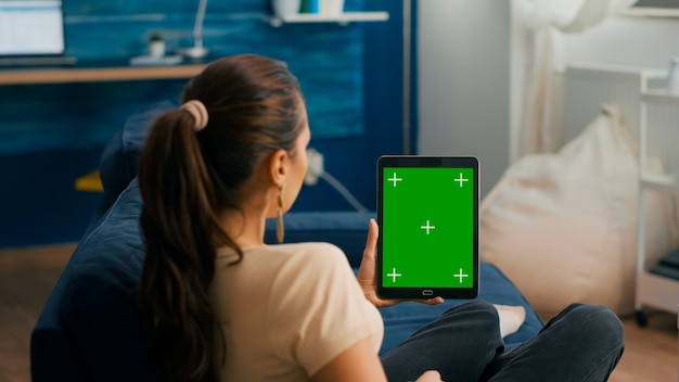 녹색 화면 크로마 키 디스플레이가 거실 소파에 앉아 있는 태블릿 컴퓨터를 보고 있는 비즈니스 여성. 소셜 네트워크 탐색을 위해 격리된 터치스크린 장치를 사용하는 프리랜서