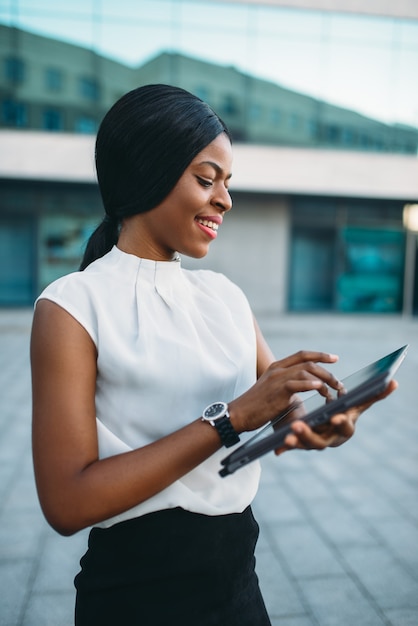 Business woman looks on laptop screen in front of office building.