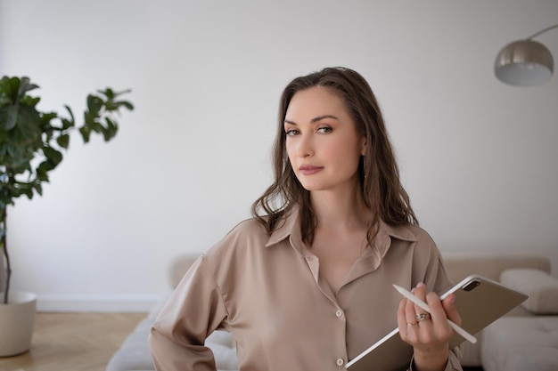 A business woman in a loose beige suit holds a digital tablet in her hands a photo in the interior c