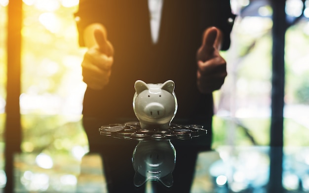 Photo a business woman making and showing thumbs up hand sign with piggy bank and coins on the table for saving money concept