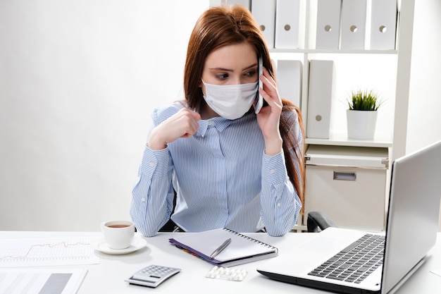business woman in a mask at the workplace talking on the phone