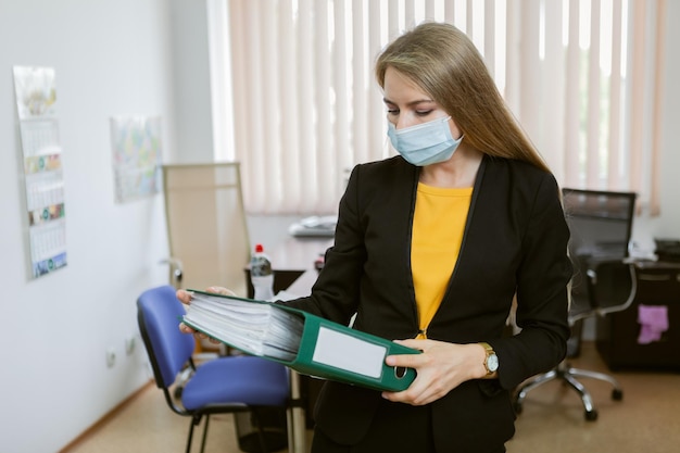 Business woman in medical mask holding folder in office