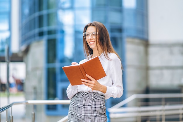 Business woman outdoors near modern business center with notebook.