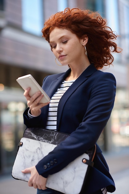 Business woman phone and walking in the city for communication social media or texting and chatting Female ginger typing on smartphone taking walk with 5G connection mobile app or travel in town