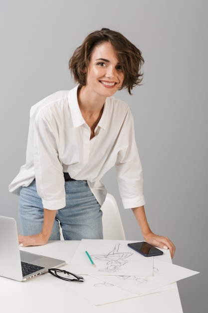 Foto donna di affari in posa isolato sopra il muro grigio al tavolo vicino al computer portatile