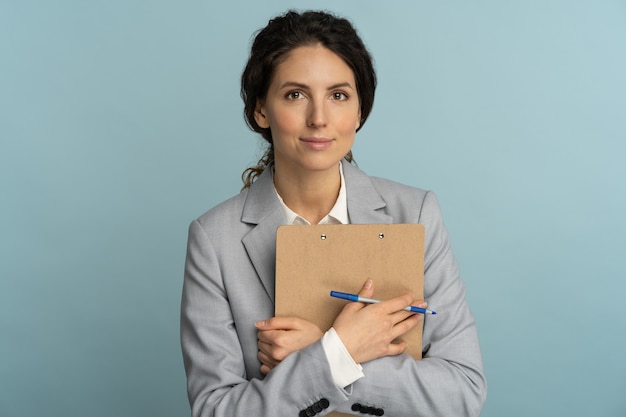Business woman presses clipboard to itself and looking at camera.