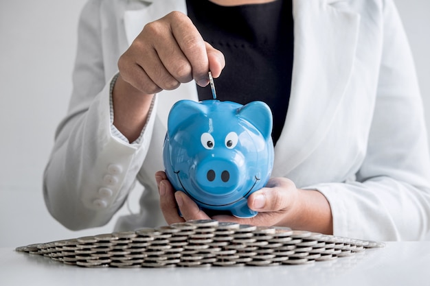 Business woman putting coin into blue piggy bank for planning step up growing business to profit and saving with piggy bankfund concept