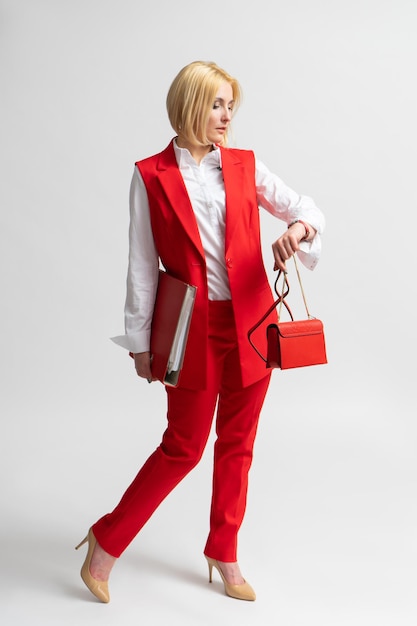 Business woman in a red suit with an office folder and a handbag looks at her watch