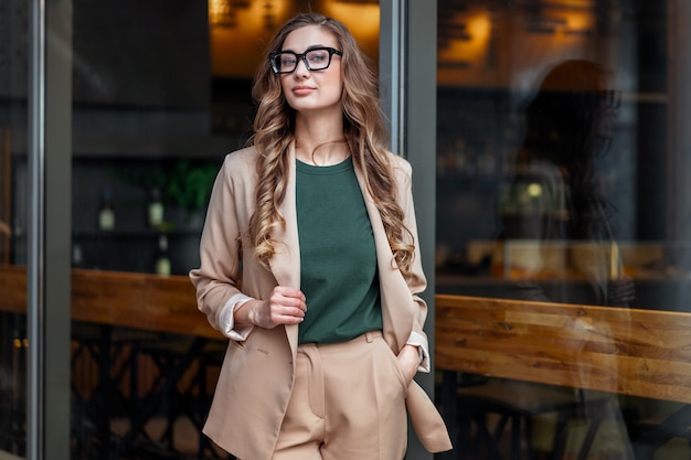 Деловая женщина, владелец ресторана, одетая в элегантный брючный костюм, стоит возле ресторана с большим окном на открытом воздухе, кавказские женские очки, деловой человек