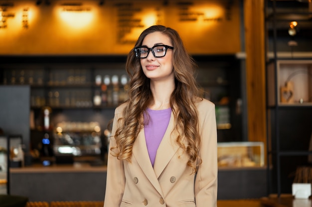 Donna d'affari proprietario del ristorante vestito elegante pantalone in piedi nel ristorante con bancone bar sfondo femmina caucasica occhiali persona d'affari indoor