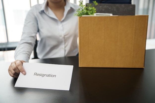 Photo business woman sending resignation letter to boss and holding stuff resign depress or carrying cardboard box by desk in office