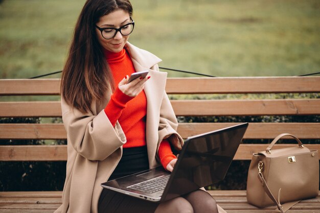 Business woman sitting on a bench with laptop and phone