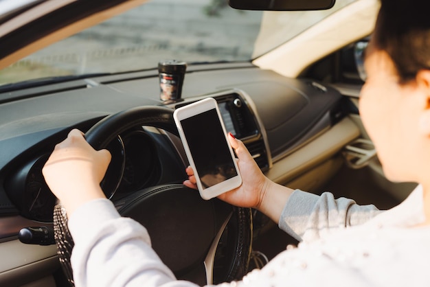 Business woman sitting in car and using her smartphone. Mockup image with female driver and phone screen