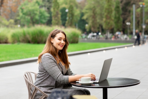 Business woman sitting in a coffee shop on the street, working at a laptop.