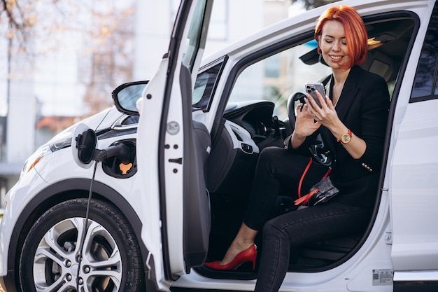 Donna d'affari seduta in auto elettrica presso la stazione di ricarica elettrica