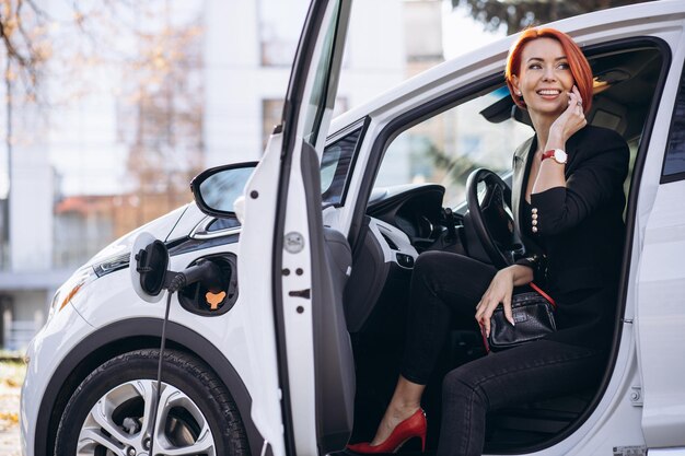 Donna d'affari seduta in auto elettrica presso la stazione di ricarica elettrica