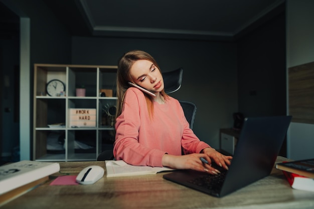 Business woman sitting at home at her desk with books and computer talking on the phone