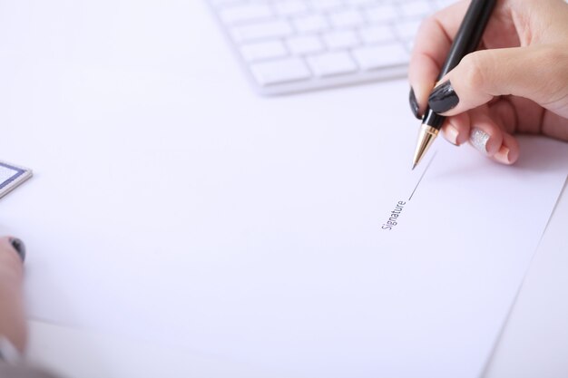 Photo business woman sitting at office desk signing a contract with shallow focus on signature.