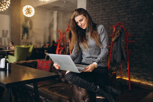 Donna di affari che si siede su un sofà con il computer portatile in un caffè