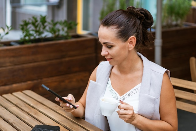 Деловая женщина сидит в уличном кафе, пьет кофе и разговаривает по телефону. Концепция перерыва на кофе