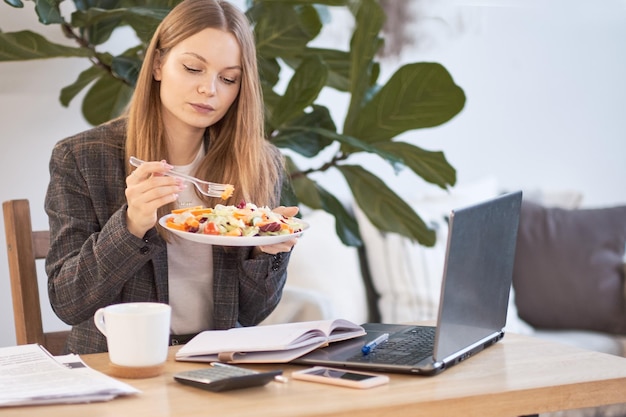 Business woman sitting with a laptop in a cafe and eating breakfast with a cup of coffee on the table