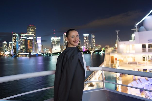 Business woman smile in suit jacket in miami, usa. Sensual woman on ship board on night skyline. Fashion, beauty, look. Travelling for business. Wanderlust, adventure, discovery, journey