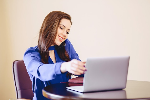 Business woman speaks by phone in office and working on laptop