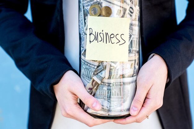 Business woman in the suit holding a bottle with money for the future investment. Close-up view on the bottle