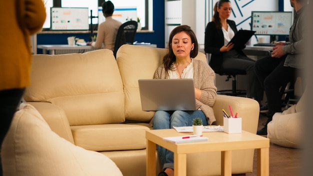 Business woman talking during video conference calling from\
laptop sitting on couch. manager executive communicating in online\
virtual chat remote meeting, looking at pc working from modern\
office.