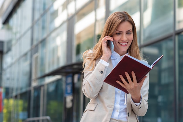 Business woman talking on phone and looking at her notebook outdoor