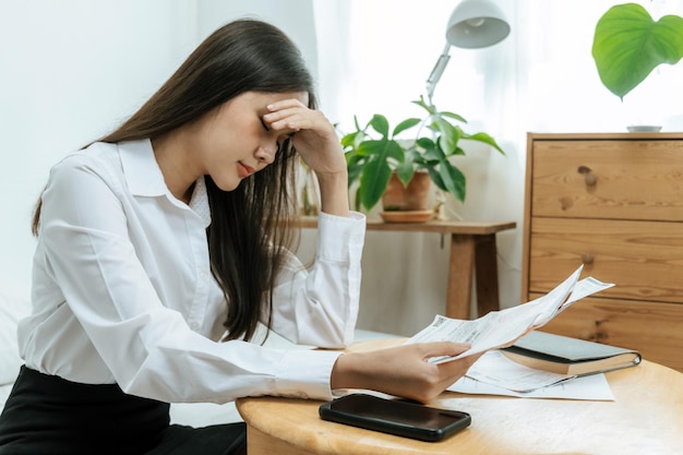 頭痛の片頭痛を抱えて額に触れるビジネスウーマンは、ホームオフィスでの請求書文書レポートにストレスを感じています。