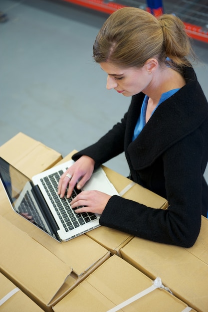 Business woman typing on laptop in warehouse