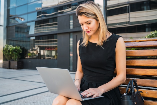 Donna di affari che per mezzo del suo computer portatile all'aperto.