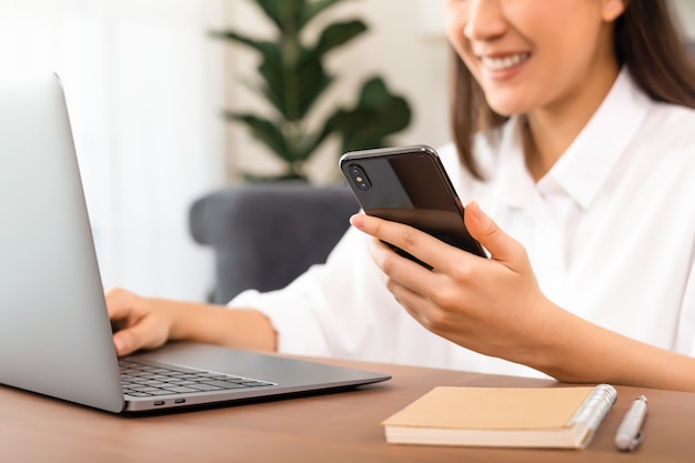 Business woman using smartphone and laptop in home office.