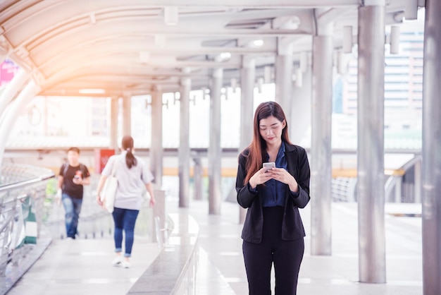 Donna d'affari che utilizza smartphone shopping online chiamata sms messaggio internet tecnologia stile di vita donna asiatica che utilizza cellulare camminando sulla strada di città smart phone smart donna sicura di sé città moderna