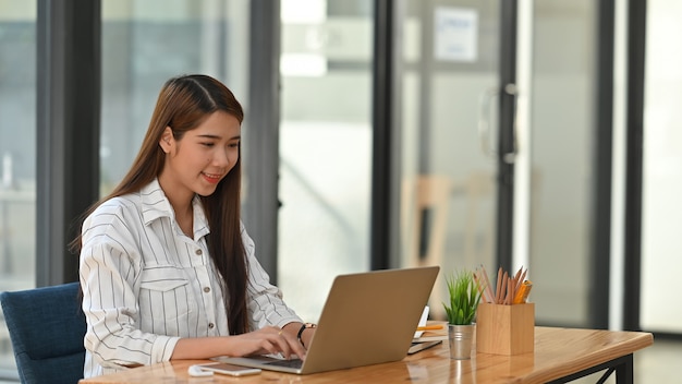 近代的なオフィスでラップトップでタイプしている間ビジネスの女性。