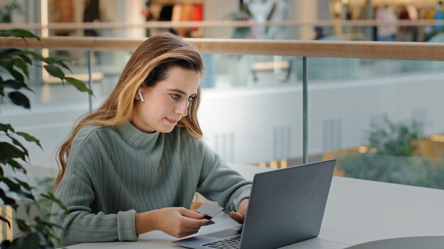 Business woman in wireless headphones girl buyer user pays website with credit card booking order