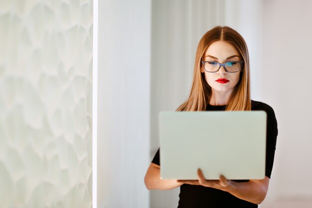 Business woman with laptop in black dress in white office