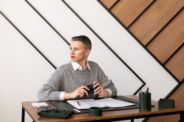 Деловая женщина с короткой стрижкой смотрит в окно, сидя за своим столом в офисе