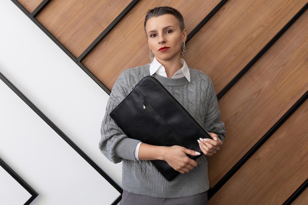 A business woman with a short haircut stands with a folder for documents on the background of a wall