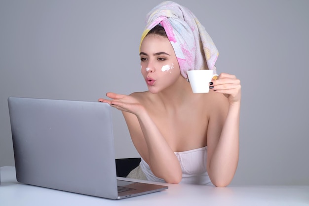 Business woman with towel on head facial cream on face hold cup of coffee working on laptop morning