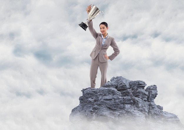 Business woman with trophy on mountain peak in the clouds