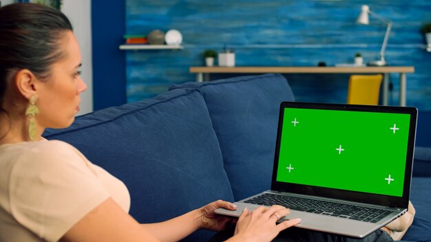 Business woman working on communication project for company uses isolated laptop computer with green screen chroma key lying on sofa in living room