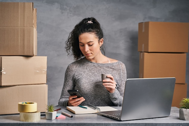 Business woman working from home with laptop and notepad preparing boxes with products for delivery