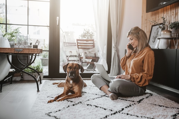 Business woman working on laptop computer sitting at home with her dog and managing her business via