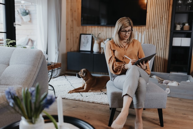 Business woman working on laptop computer sitting at home with her dog and managing her business via