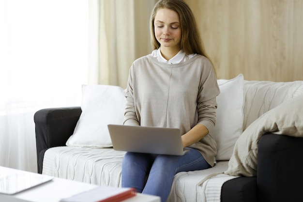 Photo business woman working on laptop computer sitting indoors during covid-19 quarantine in cozy living room. stay at home concept during coronavirus pandemic.