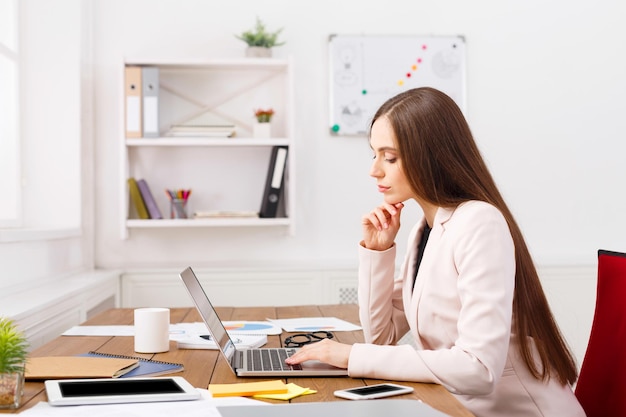 Business woman working on laptop at office and having coffee sitting at her working place, copy space, side view