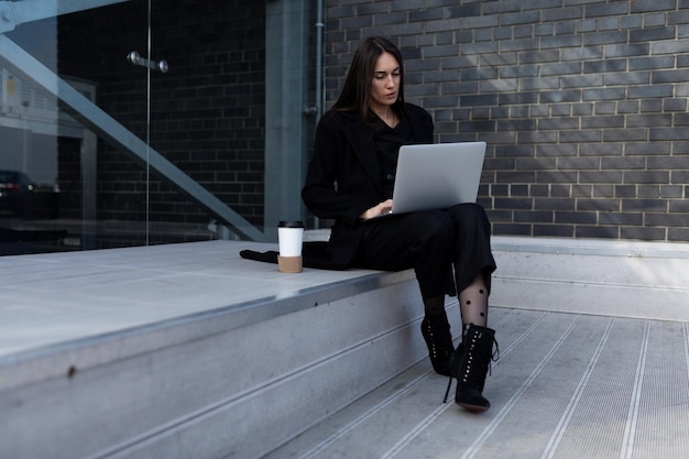 Donna di affari che lavora al computer portatile in linea che si siede sui gradini